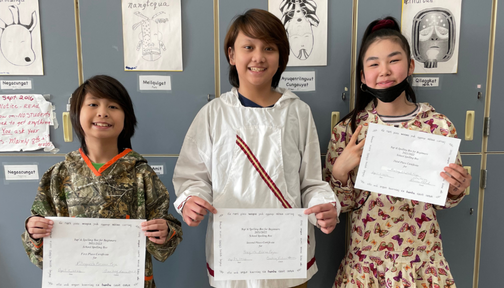 Wearing traditional Yup’ik qaspeqs, students, Pilinguasta (1st place), Naaqista (2nd place), and Airluq (3rd place), hold up their Yup’ik Spelling Bee certificates.
