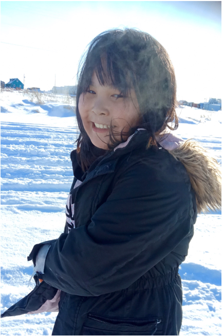 A smiling girl in a black parka standing in the snow.